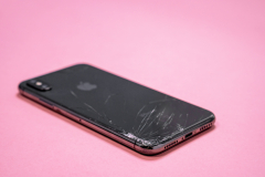 April 11, 2020, Rostov-on-Don, Russia: smartphone iPhone X of space grey color with broken back glass with cracks and damages on pink background, side view, selective focus